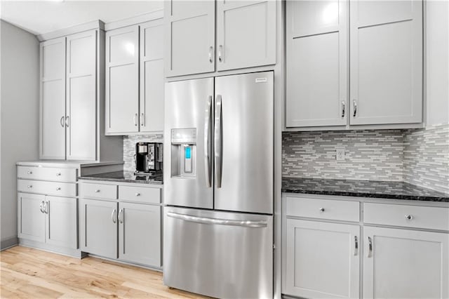 kitchen with backsplash, dark stone countertops, light hardwood / wood-style flooring, and stainless steel refrigerator with ice dispenser