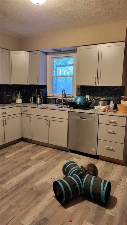 kitchen featuring white cabinets, a textured ceiling, tasteful backsplash, stainless steel dishwasher, and light hardwood / wood-style flooring