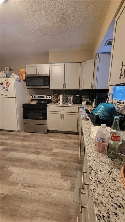 kitchen with white cabinetry, light wood-type flooring, appliances with stainless steel finishes, and light stone counters