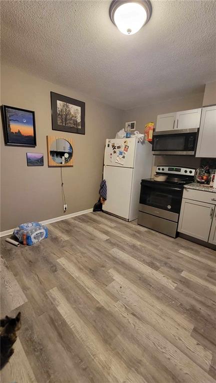 kitchen with stainless steel appliances, light hardwood / wood-style floors, white cabinetry, and a textured ceiling