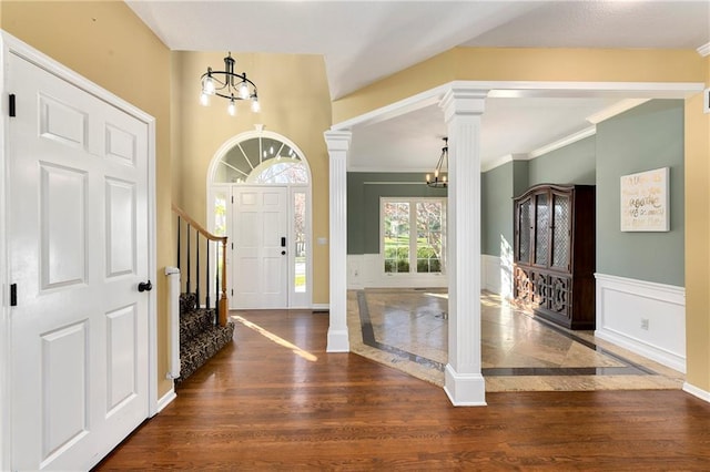 entryway with a chandelier, dark wood-style flooring, stairs, wainscoting, and decorative columns