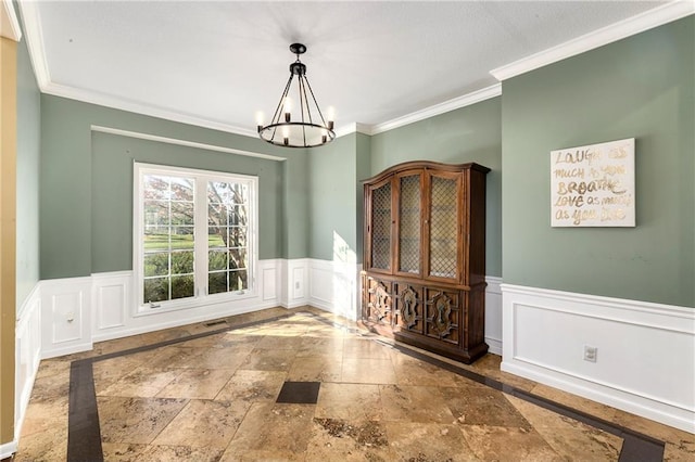 unfurnished dining area featuring visible vents, wainscoting, stone tile flooring, crown molding, and a notable chandelier