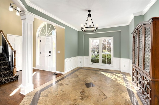 foyer entrance with a wainscoted wall, crown molding, an inviting chandelier, ornate columns, and stairs