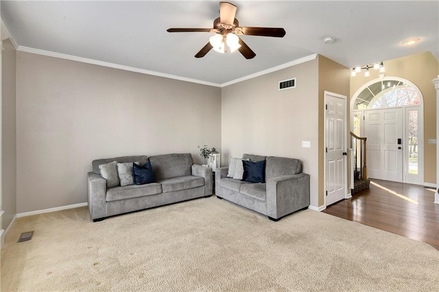 living area with baseboards, visible vents, a ceiling fan, and ornamental molding