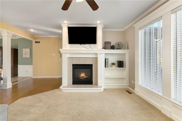 unfurnished living room featuring a tile fireplace, visible vents, crown molding, and decorative columns