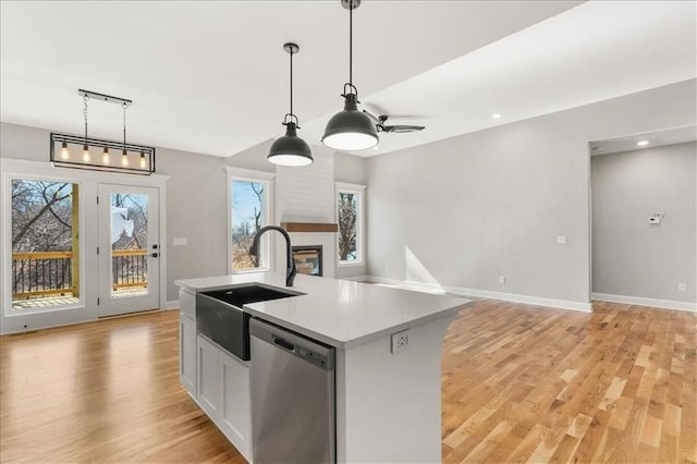 kitchen featuring a center island with sink, stainless steel dishwasher, light hardwood / wood-style flooring, sink, and decorative light fixtures