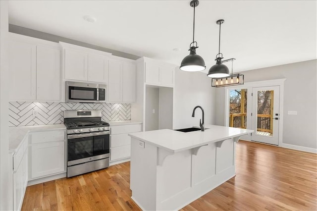 kitchen with sink, white cabinetry, stainless steel appliances, pendant lighting, and a kitchen island with sink