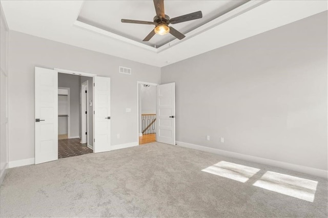 unfurnished bedroom with a raised ceiling, a walk in closet, carpet, and ceiling fan