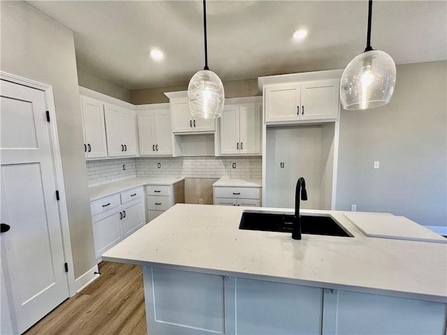 kitchen with light wood finished floors, decorative backsplash, a kitchen island with sink, and a sink