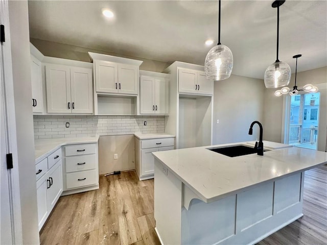 kitchen featuring a sink, light wood-style floors, a kitchen island with sink, and white cabinets