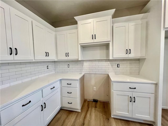 kitchen with white cabinetry, decorative backsplash, wood finished floors, and light countertops