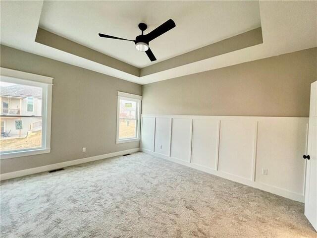 unfurnished room featuring visible vents, a tray ceiling, light carpet, a decorative wall, and a ceiling fan