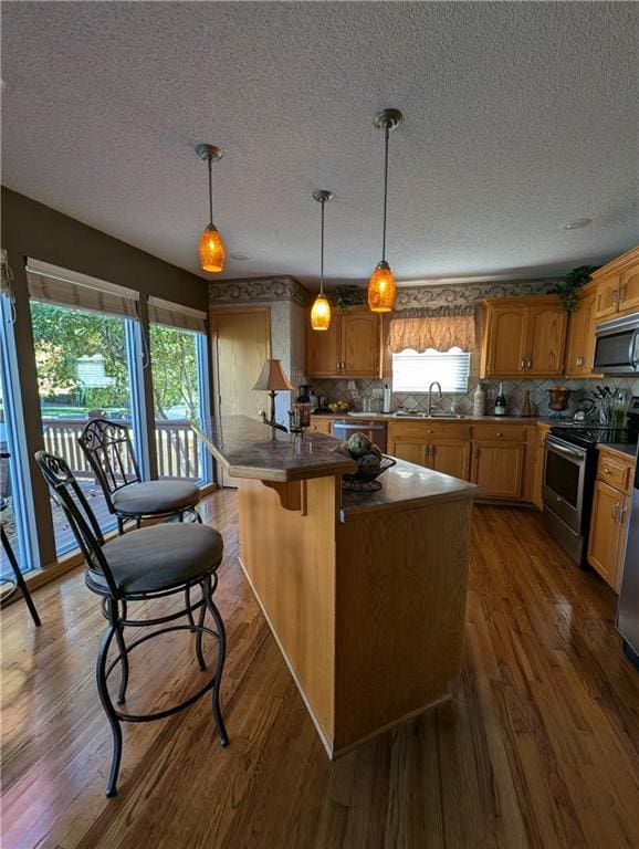 kitchen with hanging light fixtures, stainless steel appliances, plenty of natural light, and dark wood-type flooring