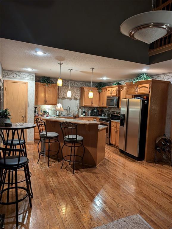 kitchen featuring hanging light fixtures, light hardwood / wood-style flooring, appliances with stainless steel finishes, tasteful backsplash, and a kitchen bar