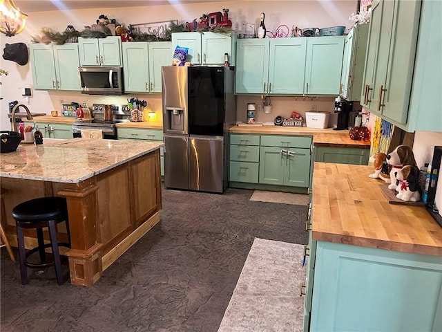 kitchen featuring stainless steel appliances, butcher block counters, a breakfast bar, a sink, and green cabinets