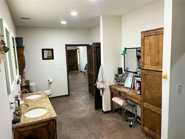 bathroom with toilet, double vanity, baseboards, and a sink