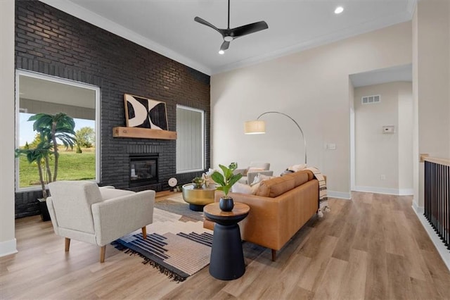 living room featuring crown molding, ceiling fan, a fireplace, and light hardwood / wood-style floors