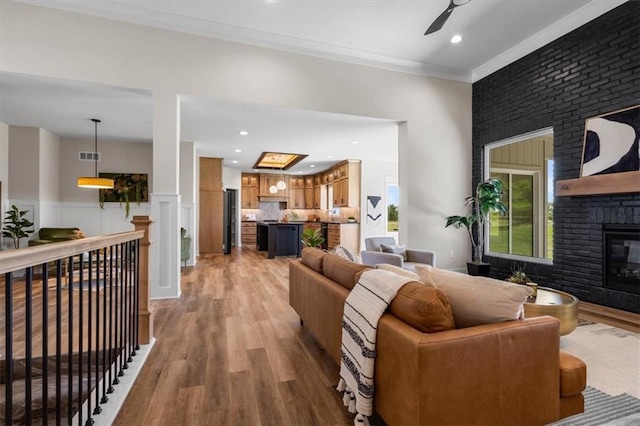 living room with ceiling fan, ornamental molding, a fireplace, and light hardwood / wood-style flooring