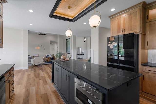 kitchen featuring pendant lighting, black appliances, a kitchen island, a raised ceiling, and light wood-type flooring