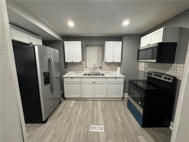 kitchen with sink, tasteful backsplash, light hardwood / wood-style flooring, white cabinets, and appliances with stainless steel finishes