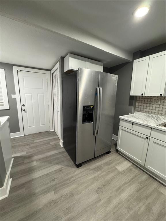 kitchen featuring white cabinetry, tasteful backsplash, light stone counters, stainless steel fridge, and light hardwood / wood-style floors