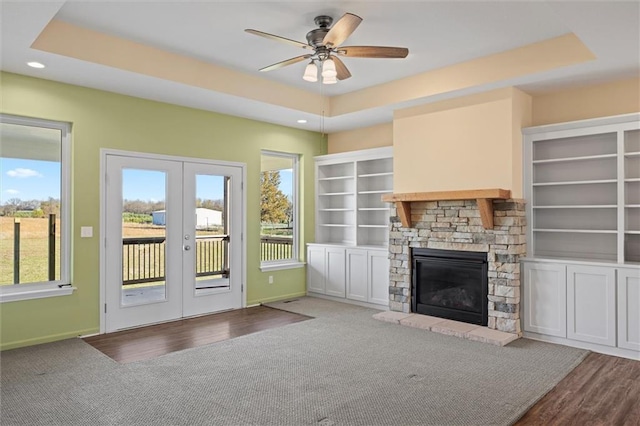 unfurnished living room with french doors, a stone fireplace, hardwood / wood-style flooring, ceiling fan, and a tray ceiling