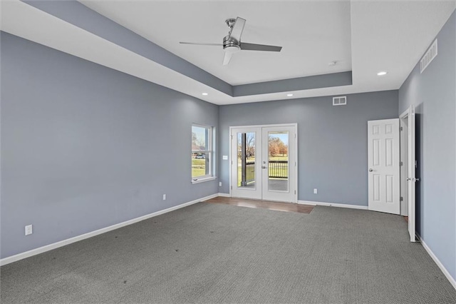 carpeted spare room with ceiling fan, a raised ceiling, and french doors