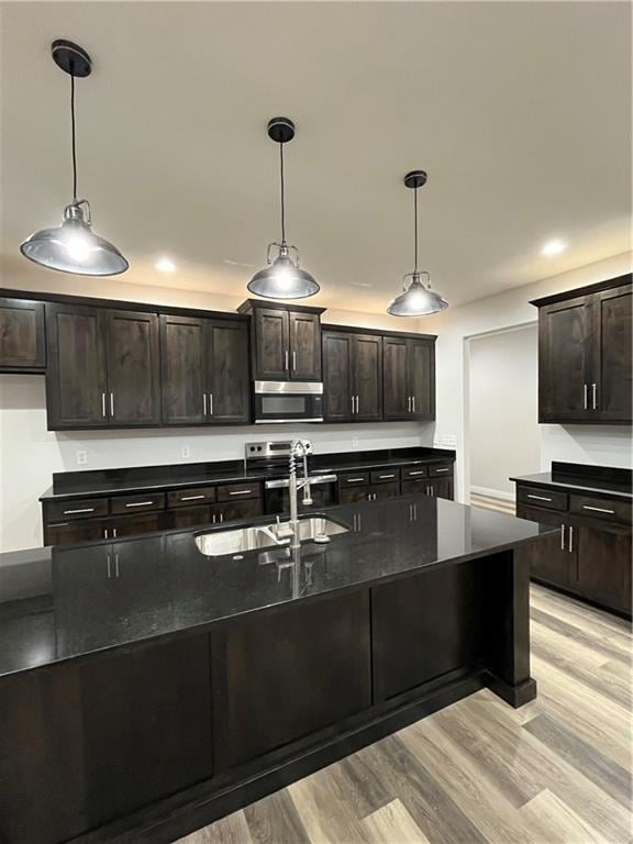 kitchen with stainless steel appliances, light wood-type flooring, dark brown cabinets, hanging light fixtures, and sink