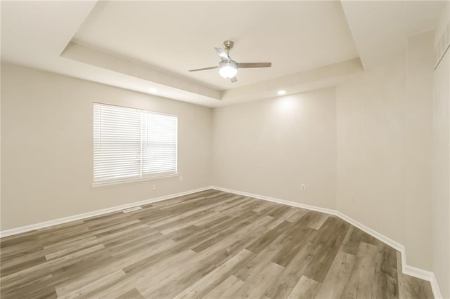 spare room with hardwood / wood-style floors, ceiling fan, and a raised ceiling