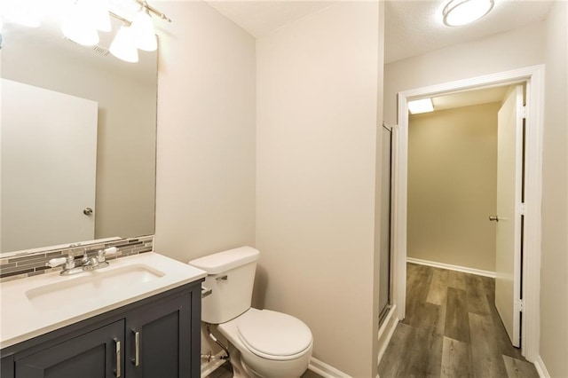 bathroom with toilet, decorative backsplash, hardwood / wood-style flooring, an enclosed shower, and vanity