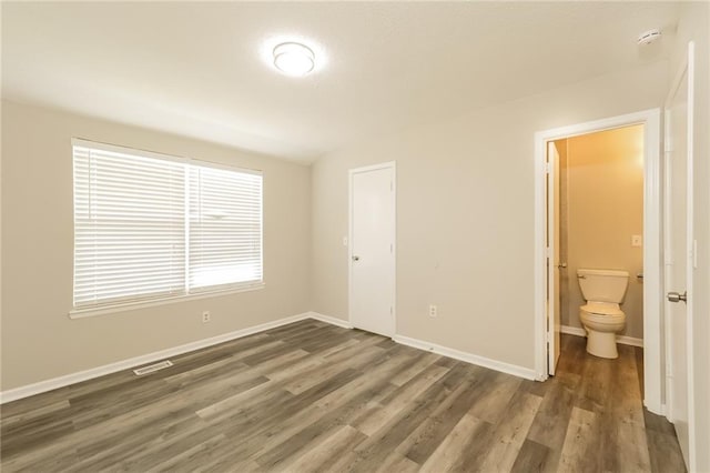 unfurnished bedroom with dark wood-type flooring, ensuite bath, and a closet