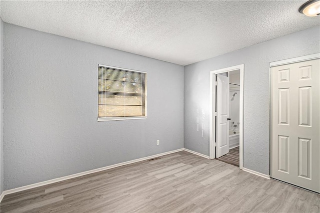 unfurnished bedroom with a closet, ensuite bath, a textured ceiling, and light hardwood / wood-style flooring