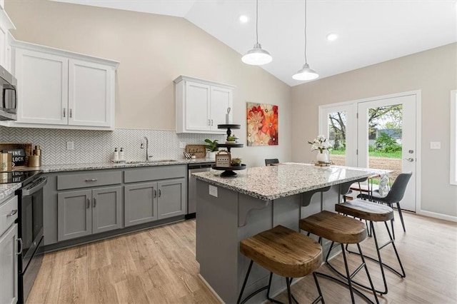 kitchen with lofted ceiling, light wood finished floors, a sink, stainless steel appliances, and gray cabinets