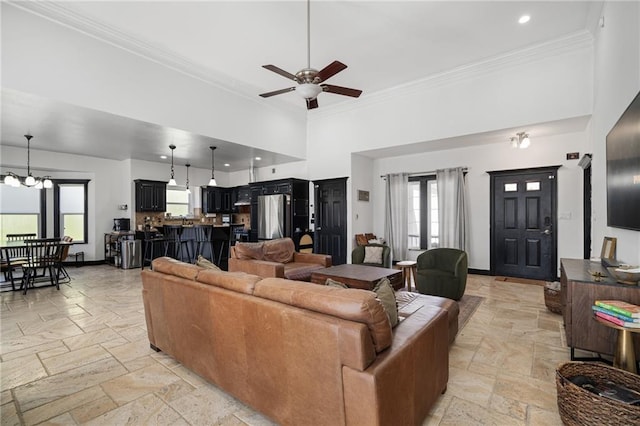 living room with crown molding, stone tile floors, a high ceiling, baseboards, and ceiling fan with notable chandelier