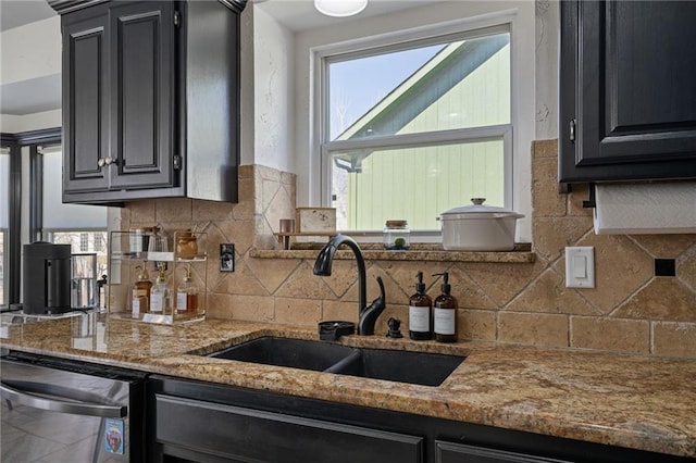 kitchen featuring tasteful backsplash, a sink, dark cabinetry, and light stone countertops