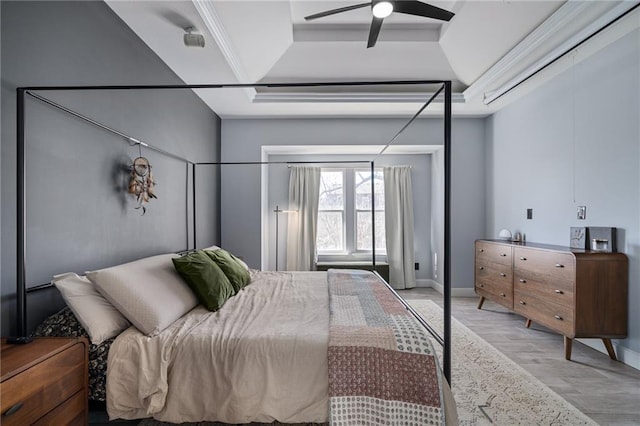 bedroom featuring a ceiling fan, baseboards, ornamental molding, a tray ceiling, and light wood finished floors