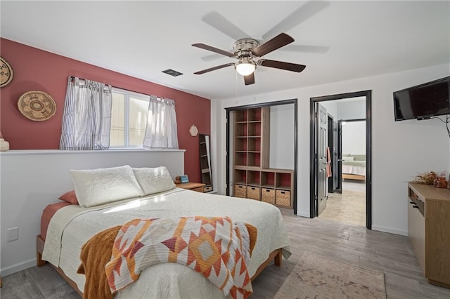 bedroom with a ceiling fan, visible vents, baseboards, and wood finished floors