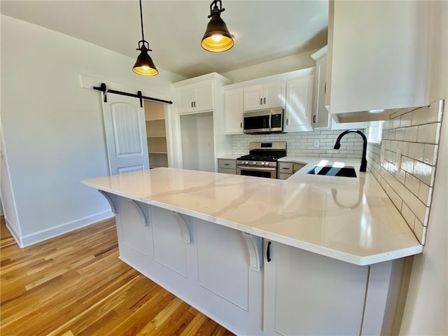 kitchen with white cabinets, sink, a barn door, appliances with stainless steel finishes, and decorative light fixtures