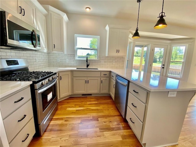 kitchen featuring stainless steel appliances, sink, light hardwood / wood-style flooring, white cabinetry, and hanging light fixtures