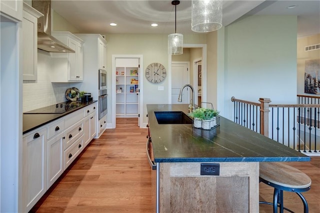 kitchen featuring white cabinetry, sink, a large island, black electric cooktop, and wall chimney exhaust hood