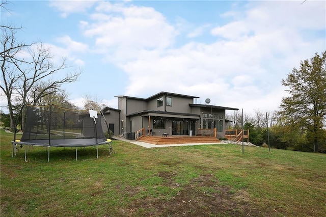 rear view of house with a deck, a lawn, and a trampoline