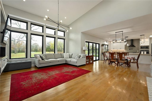 living room with high vaulted ceiling, a chandelier, and light wood-type flooring