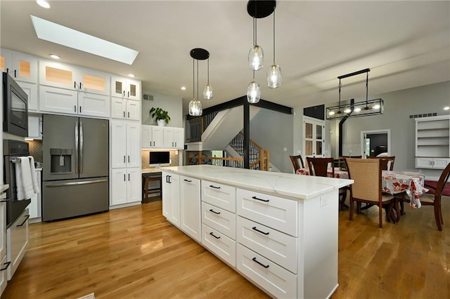 kitchen with a center island, white cabinets, black appliances, a skylight, and pendant lighting