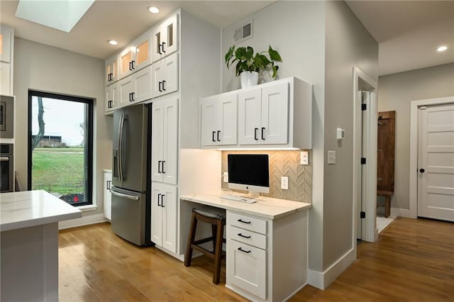 kitchen with stainless steel appliances, built in desk, light stone counters, light hardwood / wood-style flooring, and white cabinets