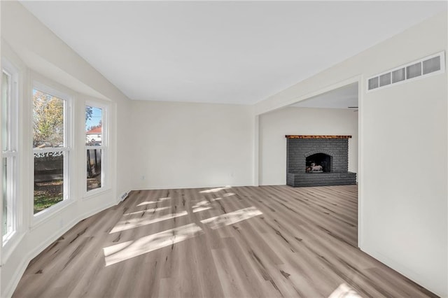 unfurnished living room with a brick fireplace and light hardwood / wood-style flooring