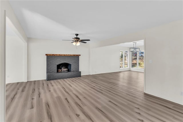 unfurnished living room featuring ceiling fan with notable chandelier, light hardwood / wood-style floors, and a fireplace