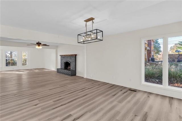 unfurnished living room with plenty of natural light, light wood-type flooring, ceiling fan with notable chandelier, and a brick fireplace