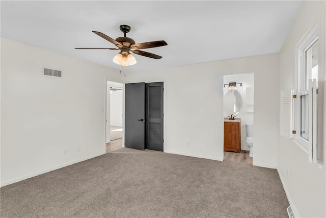 unfurnished bedroom with ensuite bathroom, a closet, ceiling fan, and light carpet