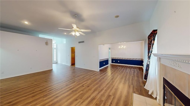 unfurnished living room with hardwood / wood-style flooring, ceiling fan with notable chandelier, and a tiled fireplace