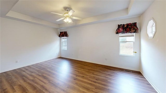 spare room with dark hardwood / wood-style floors, ceiling fan, and a raised ceiling